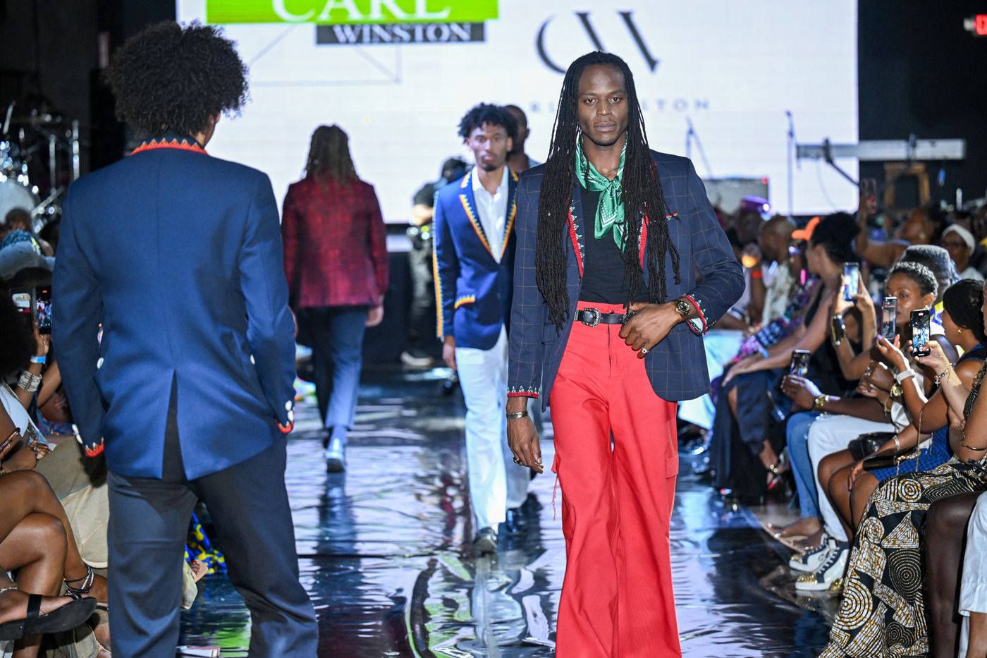 Model with locs in a green scarf and red trousers on the runway